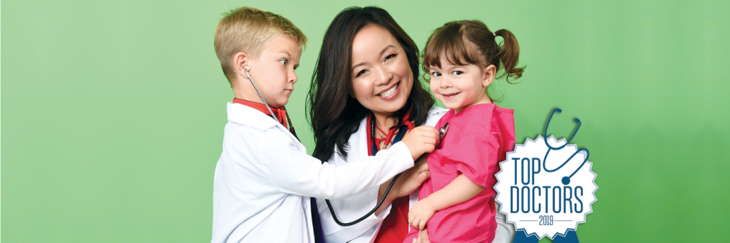 Top Doctors 2018 Banner Doctor in labcoat holding two kids, boy on left holding stethoscope to girl on right, green background