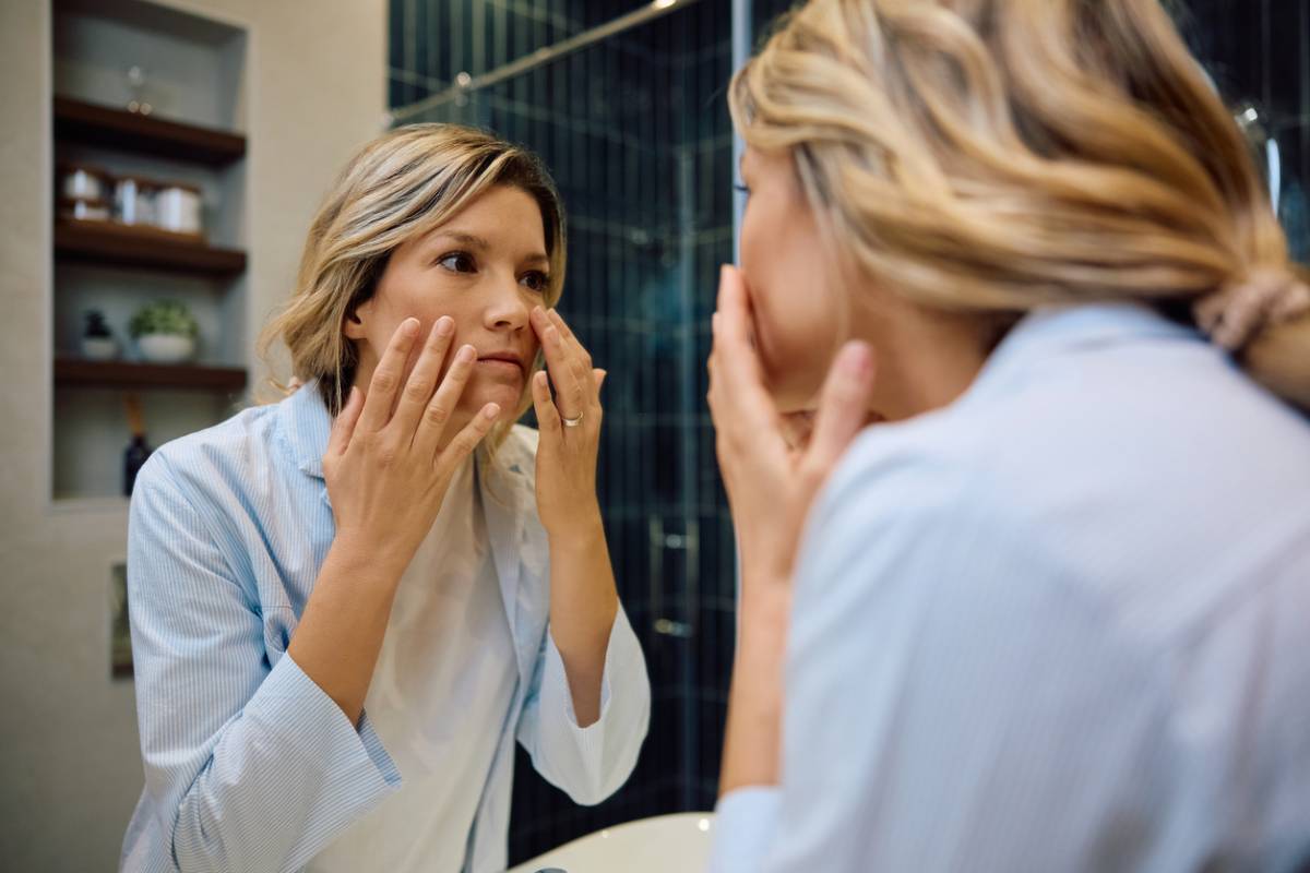 Woman looking at her under-eye circles in a mirror.